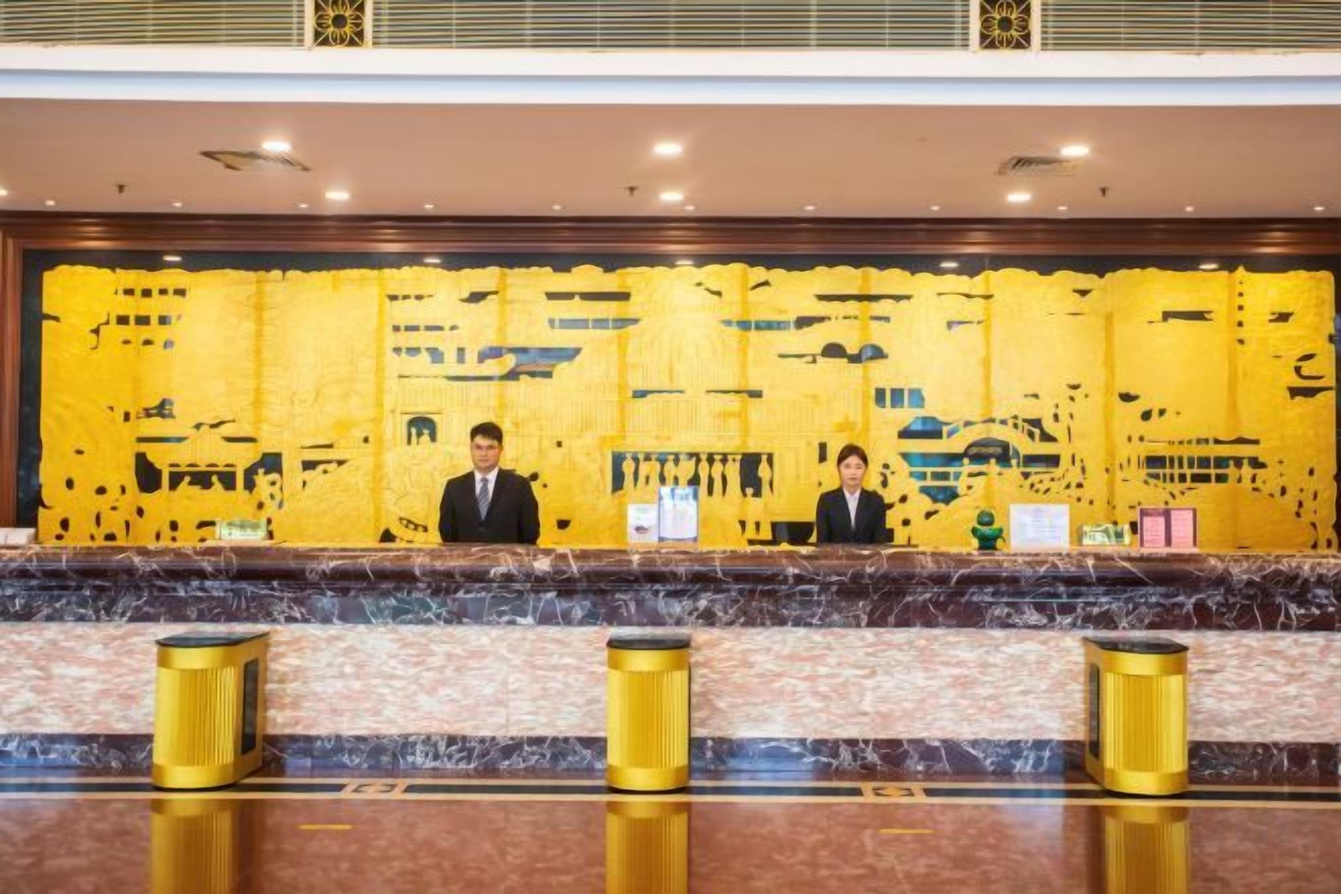 A reception desk with two staff members seated behind it, a marble counter, and three gold trash bins.