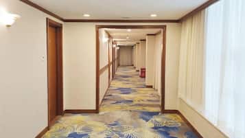 A hotel corridor with a patterned carpet, wooden doors, and a window on the right.
