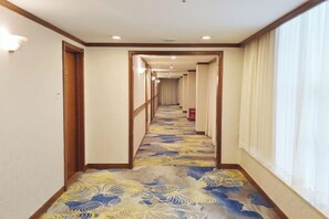 Ein Hotelgang mit Teppichmuster, Holztüren und einem Fenster auf der rechten Seite.