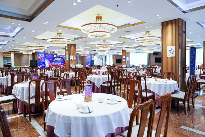 Une vaste salle de banquet avec des tables rondes et des chaises, de grands lustres et une scène en arrière-plan.