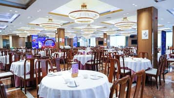 Un amplio salón de banquetes con mesas y sillas redondas, grandes candelabros y un escenario al fondo.