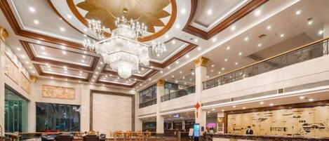 A spacious lobby with a large chandelier, a central circular design on the floor, and a reception desk.