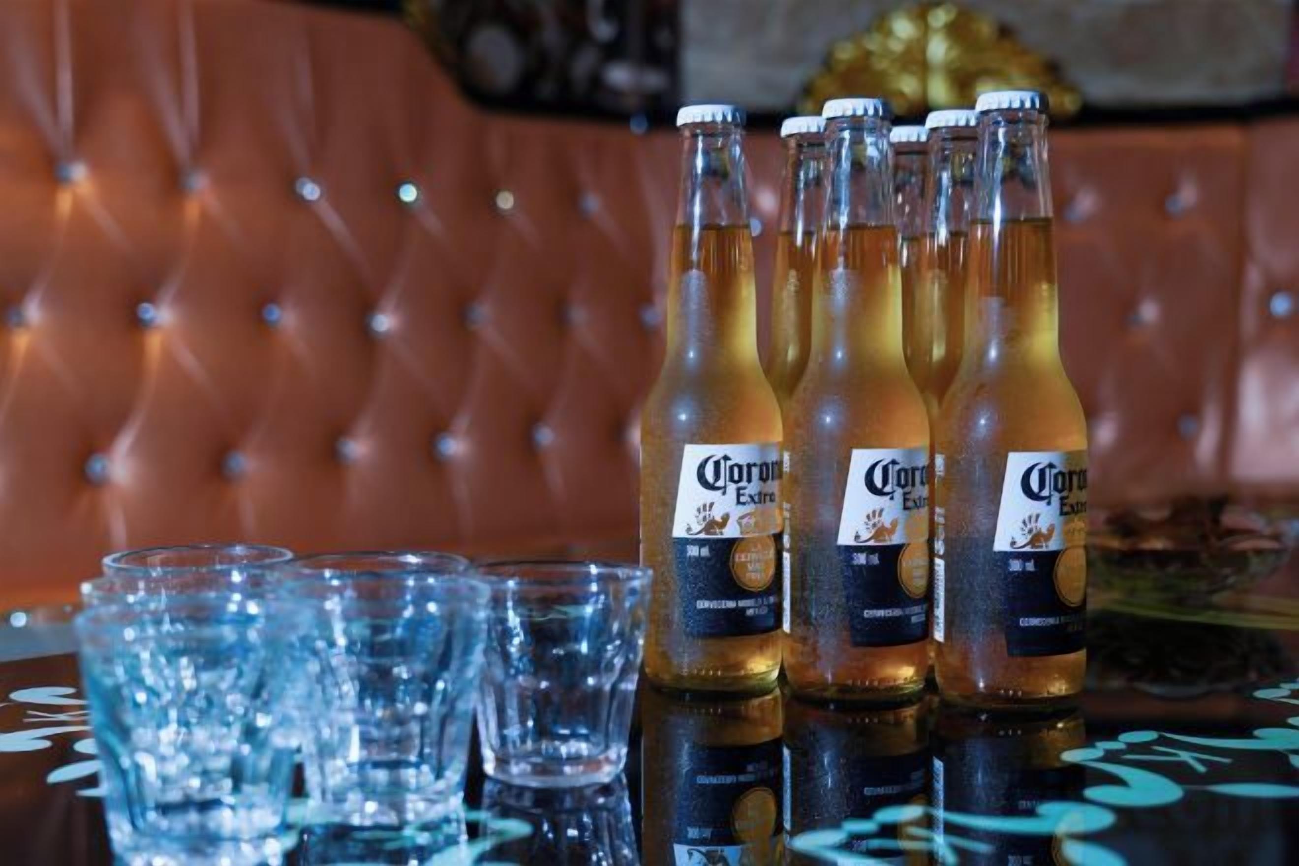 Bottles of Corona beer and empty glasses on a reflective surface.