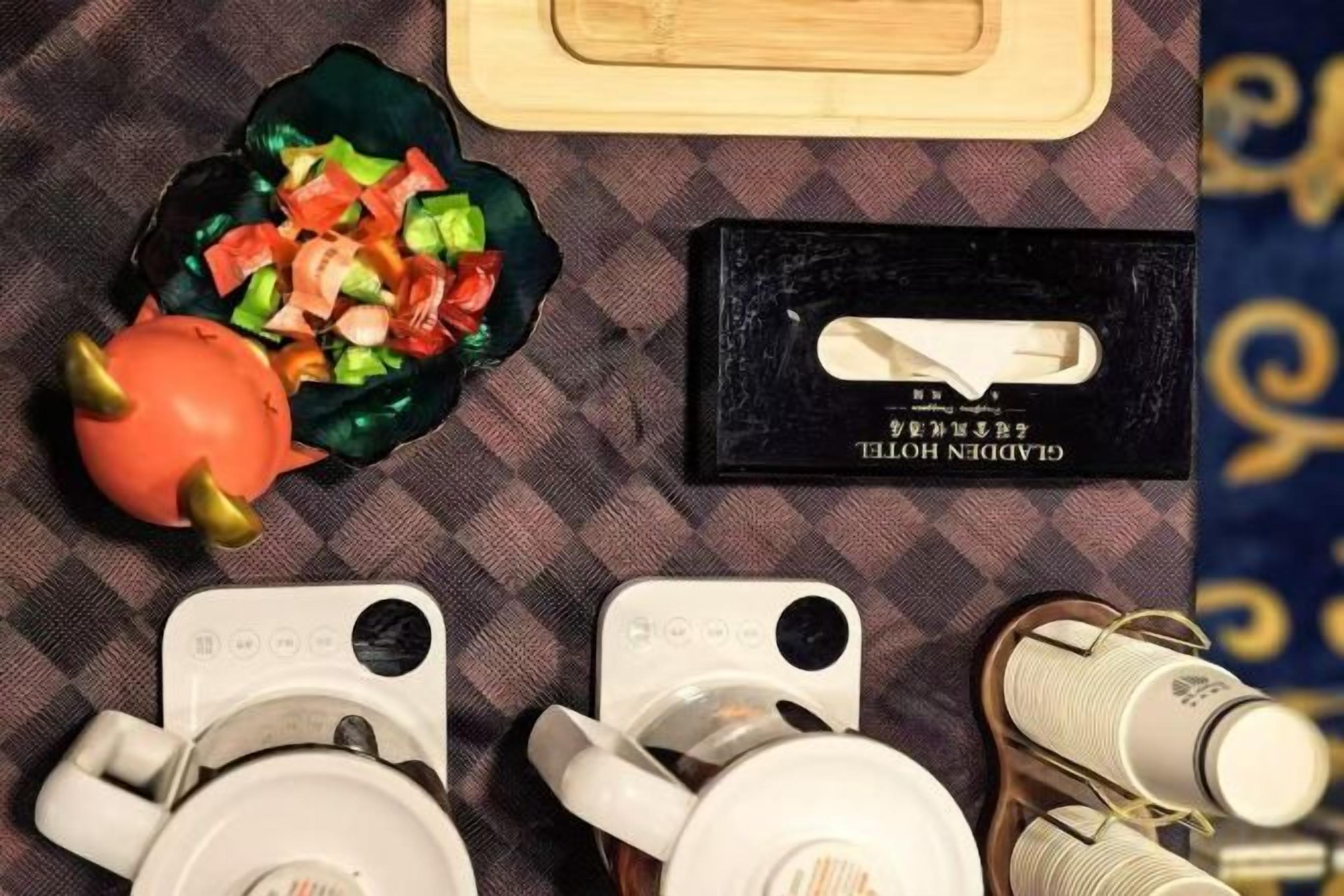 Una mesa de comedor con una ensalada, una caja negra con un asa blanco y un par de tazas blancas.