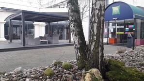 A hotel entrance with a covered outdoor seating area and a glass facade. - ibis Styles Melun Hotel (Rubelles)