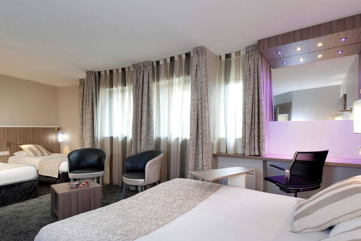 Une chambre d’hôtel avec deux lits, un bureau, une chaise et un grand miroir.