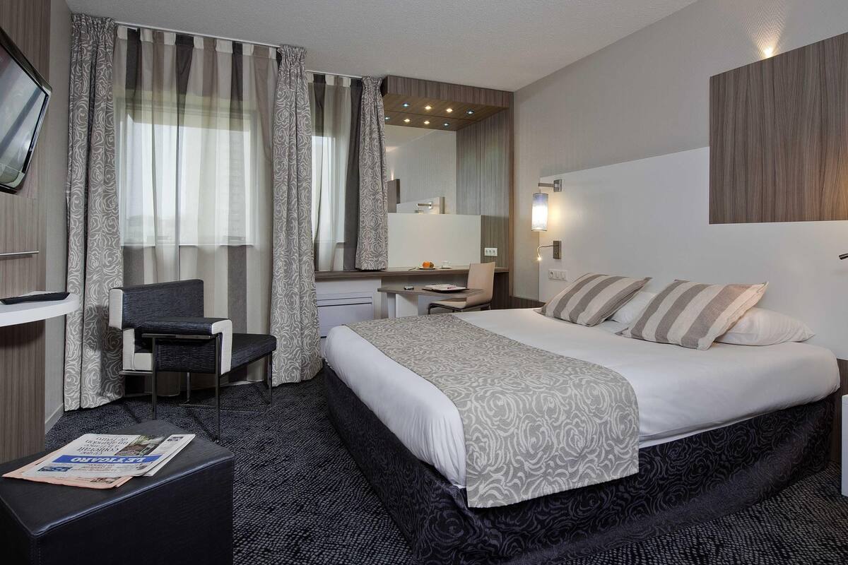 Une chambre d’hôtel avec un lit, un bureau, une chaise, une télévision et un miroir dans la salle de bain.