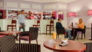 A hotel lobby with striped chairs, round tables, a bar area, and a seating area with a table and chairs.