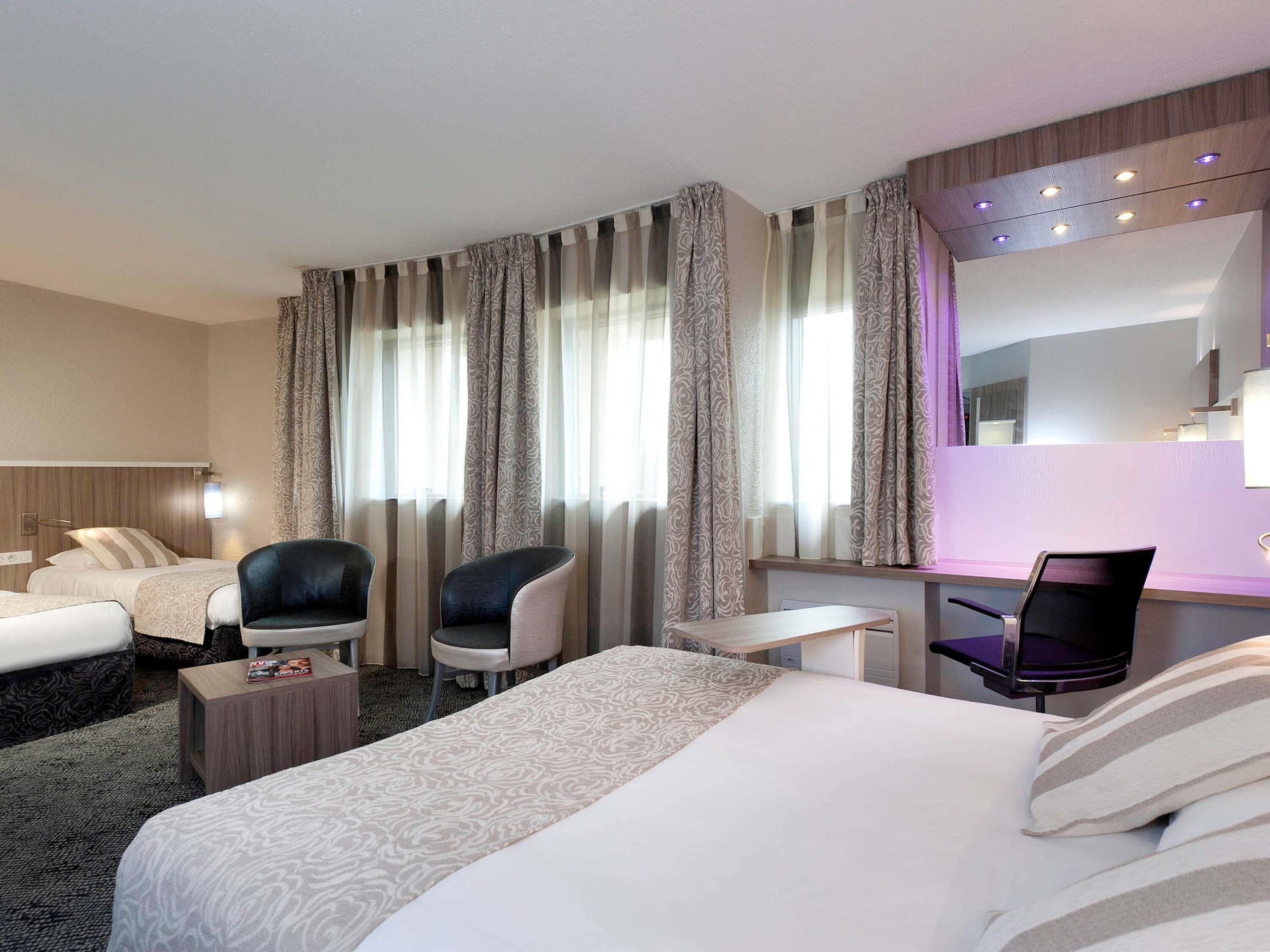 Hotellihuone, jossa on kaksi sänkyä, työpöytä, tuoli ja suuri peili.