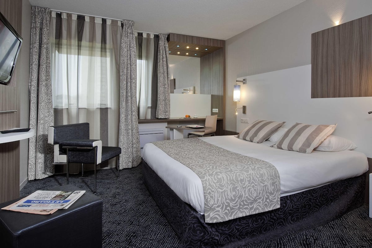 Une chambre dâhĂŽtel avec un lit, un bureau, une chaise, une tĂ©lĂ©vision et un miroir dans la salle de bain.