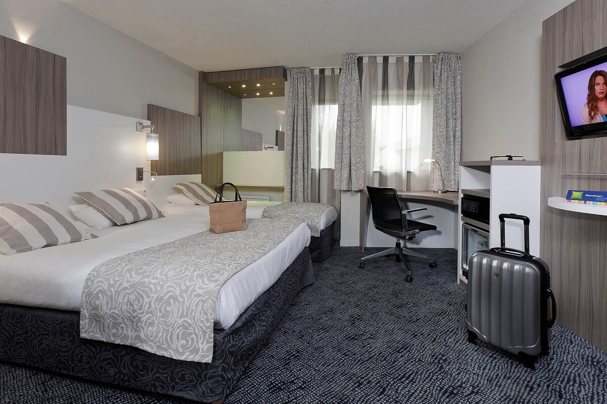Habitación de hotel con dos camas, un escritorio, una silla, un televisor y una maleta.