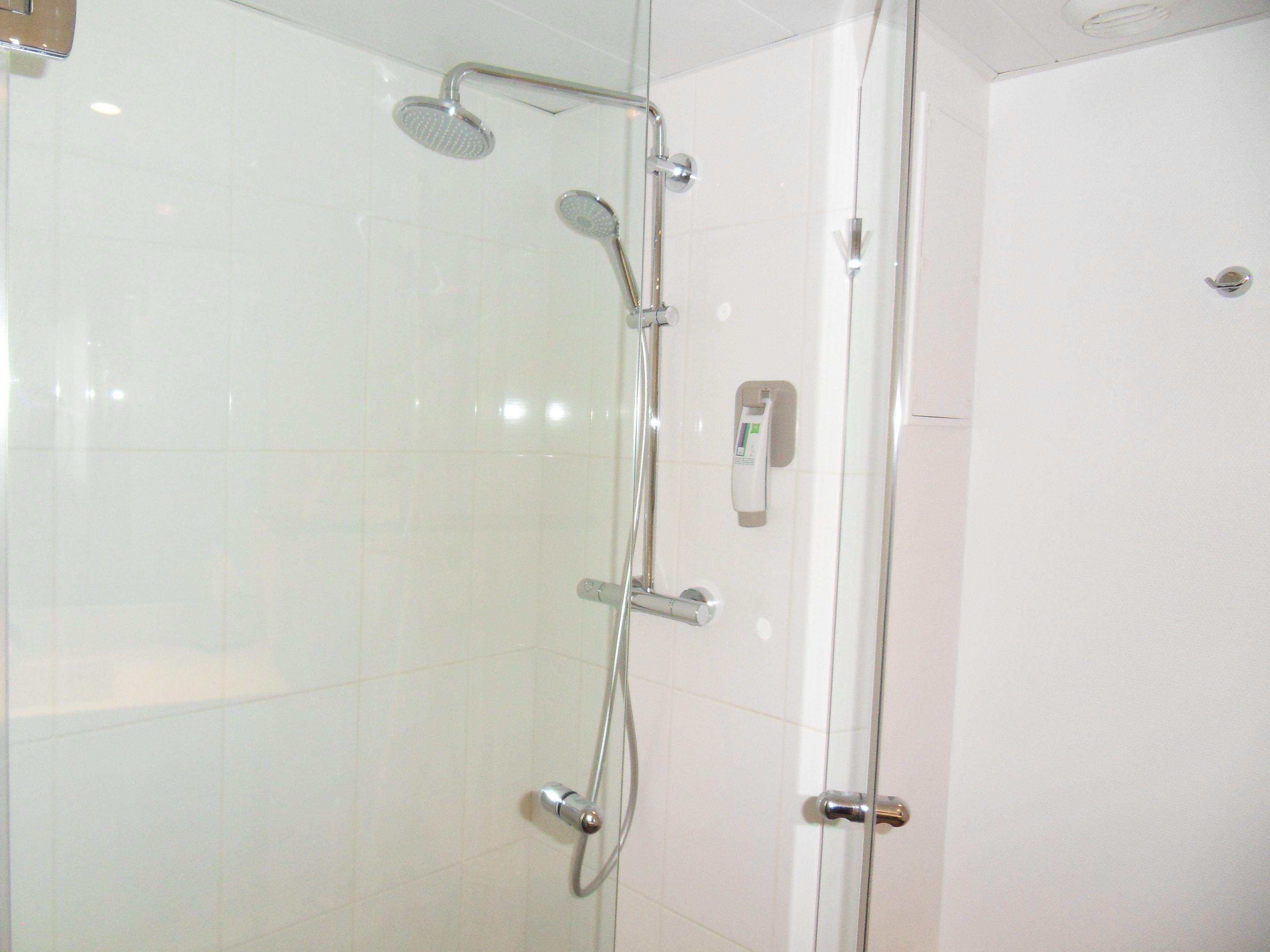 Una ducha con mampara de vidrio, cabezal de ducha de mano y panel de control en la pared.