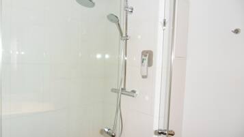Una ducha con mampara de vidrio, cabezal de ducha de mano y panel de control en la pared.