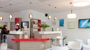 Un espace d’accueil comprenant un comptoir, un téléviseur et un coin salon avec des chaises et un tapis.