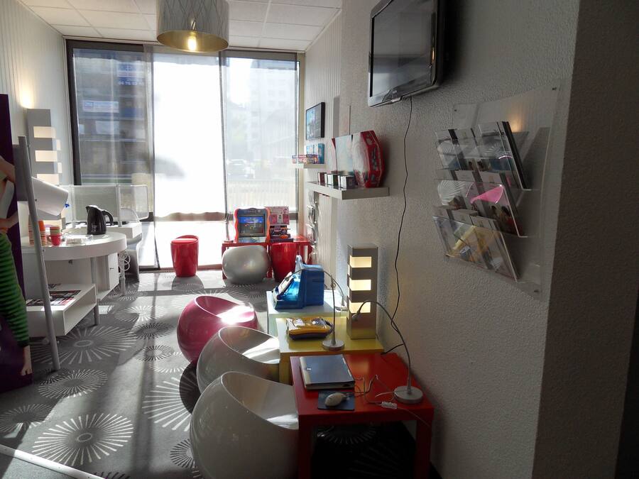 A modern living room with a large window, a flat-screen TV mounted on the wall, and a variety of seating options including a red chair and a white table.