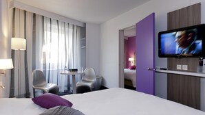 Une chambre d’hôtel comprenant un lit, une télévision, un bureau avec des chaises et une porte donnant sur une autre pièce.