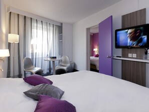 Una habitación de hotel con una cama, televisión, escritorio y sillas, además de una puerta que da a otra habitación.