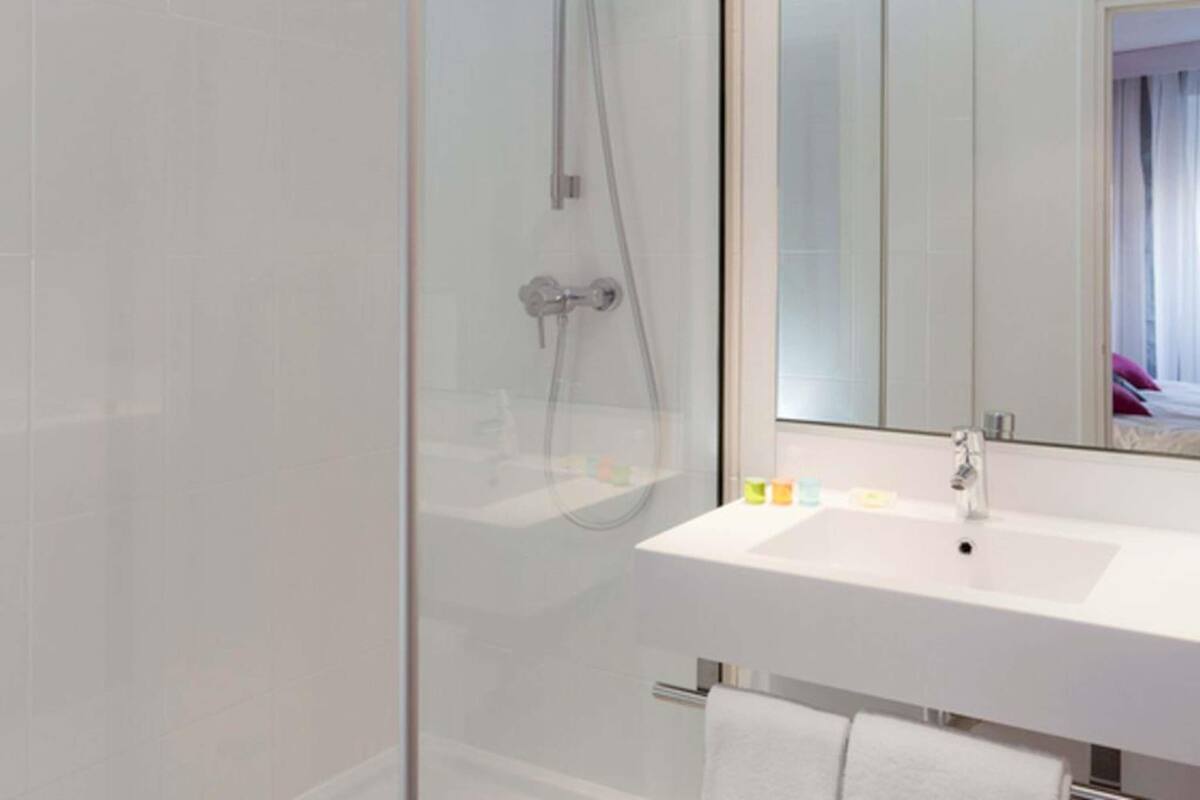 Un baño moderno con cabina de ducha de vidrio, un lavamanos blanco y un espejo grande.