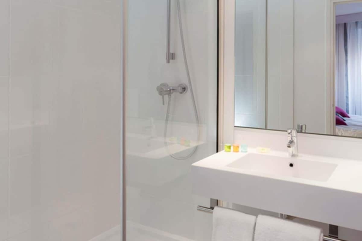 Un bagno moderno con box doccia in vetro, lavandino bianco e uno specchio grande.