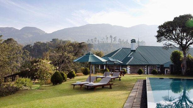 A pool area with lounge chairs and a gazebo, surrounded by well-maintained lawns and trees, with mountains in the background.