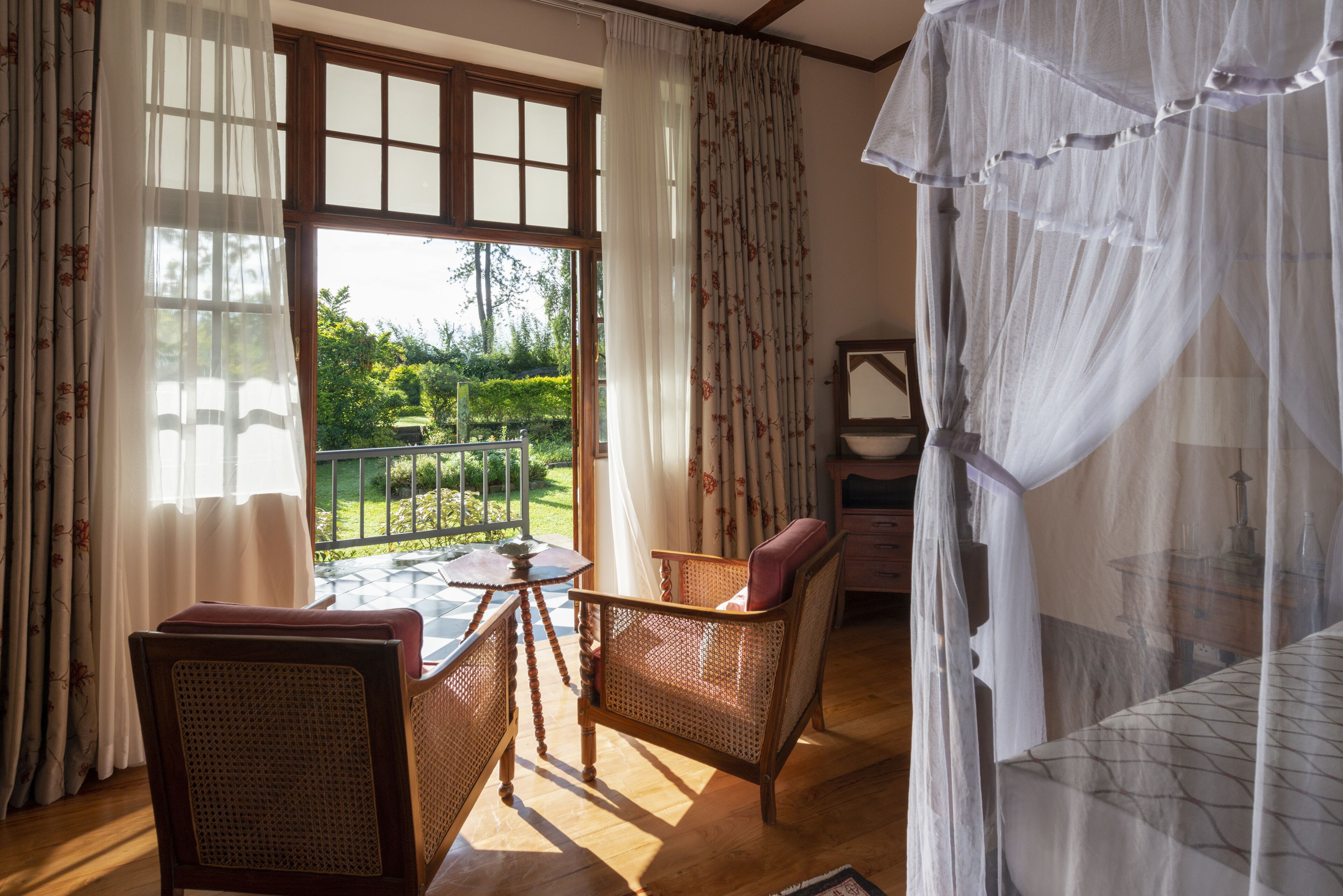 A room with a large window, wicker furniture, and a bed with a canopy.