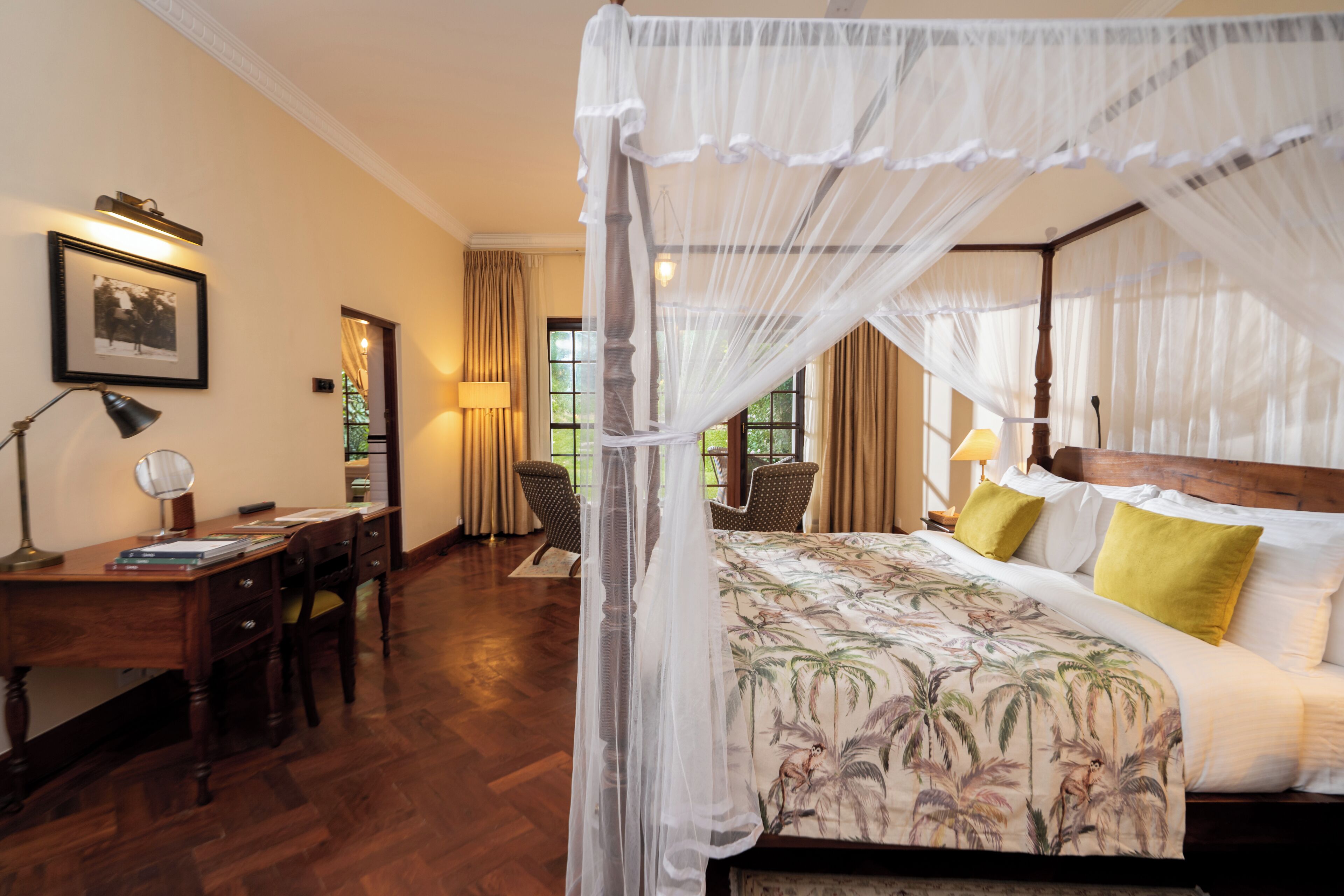A bedroom with a four-poster bed, a desk with a chair, and a window with curtains.