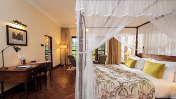 A bedroom with a four-poster bed, a desk with a chair, and a window with curtains.