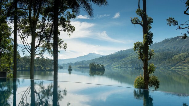A serene outdoor infinity pool with a clear view of a lake and surrounding hills.