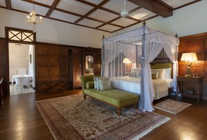 A bedroom with a four-poster canopy bed, a green sofa, and a wooden floor.