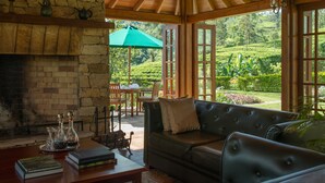A cozy room with a stone fireplace, a leather sofa, and a view of lush greenery outside.