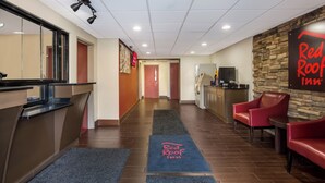 A hotel lobby with a reception desk, a Red Roof Inn sign, a kitchen area, and a seating area with red chairs.