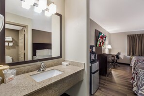 Een hotelkamer met een wastafel met granieten blad, een koelkast, een flatscreen-tv, een bed met een gestreept dekbedovertrek en een bureau met een stoel.