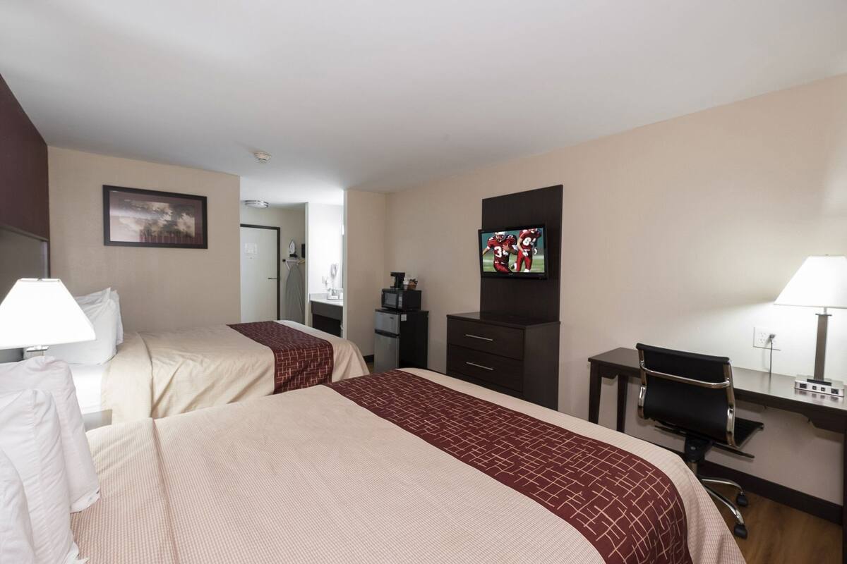 A hotel room with two beds, a desk, a television, and a chair.