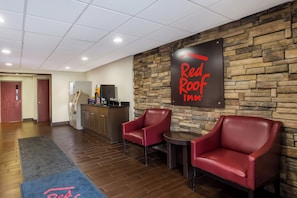 A Red Roof Inn reception area with a stone wall, a reception desk, two leather chairs, a small table, and a wooden floor. - Red Roof Inn Allentown South (Allentown)