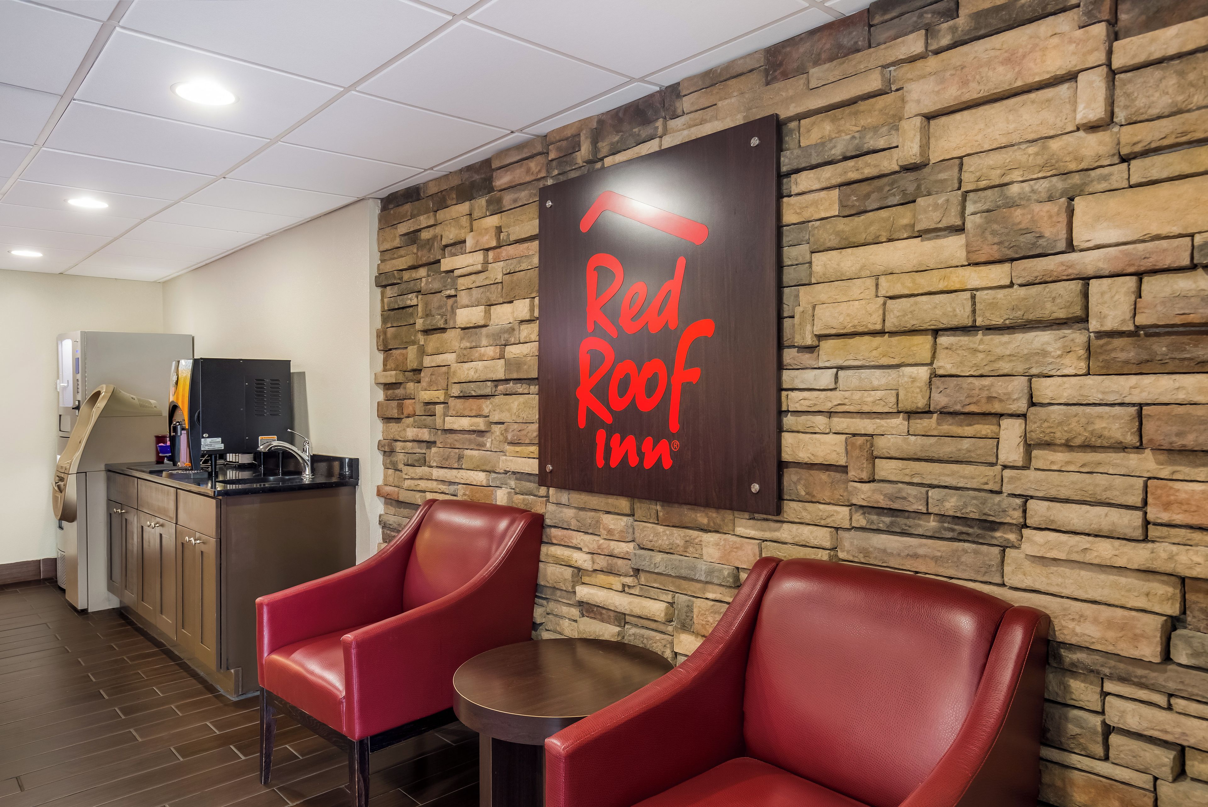 A Red Roof Inn sign, a kitchenette, and two leather chairs in a room.