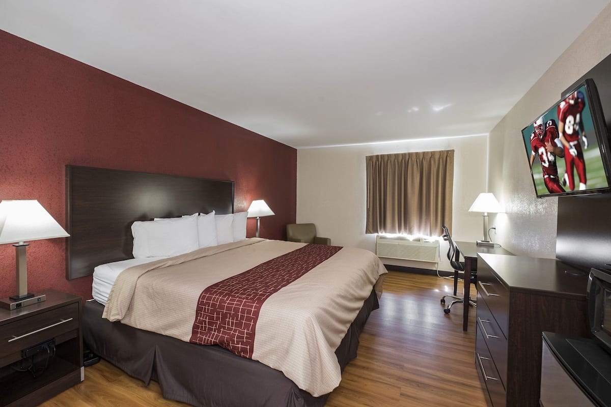 A hotel room with a bed, bedside tables, a desk, a chair, a television, and a window with curtains.