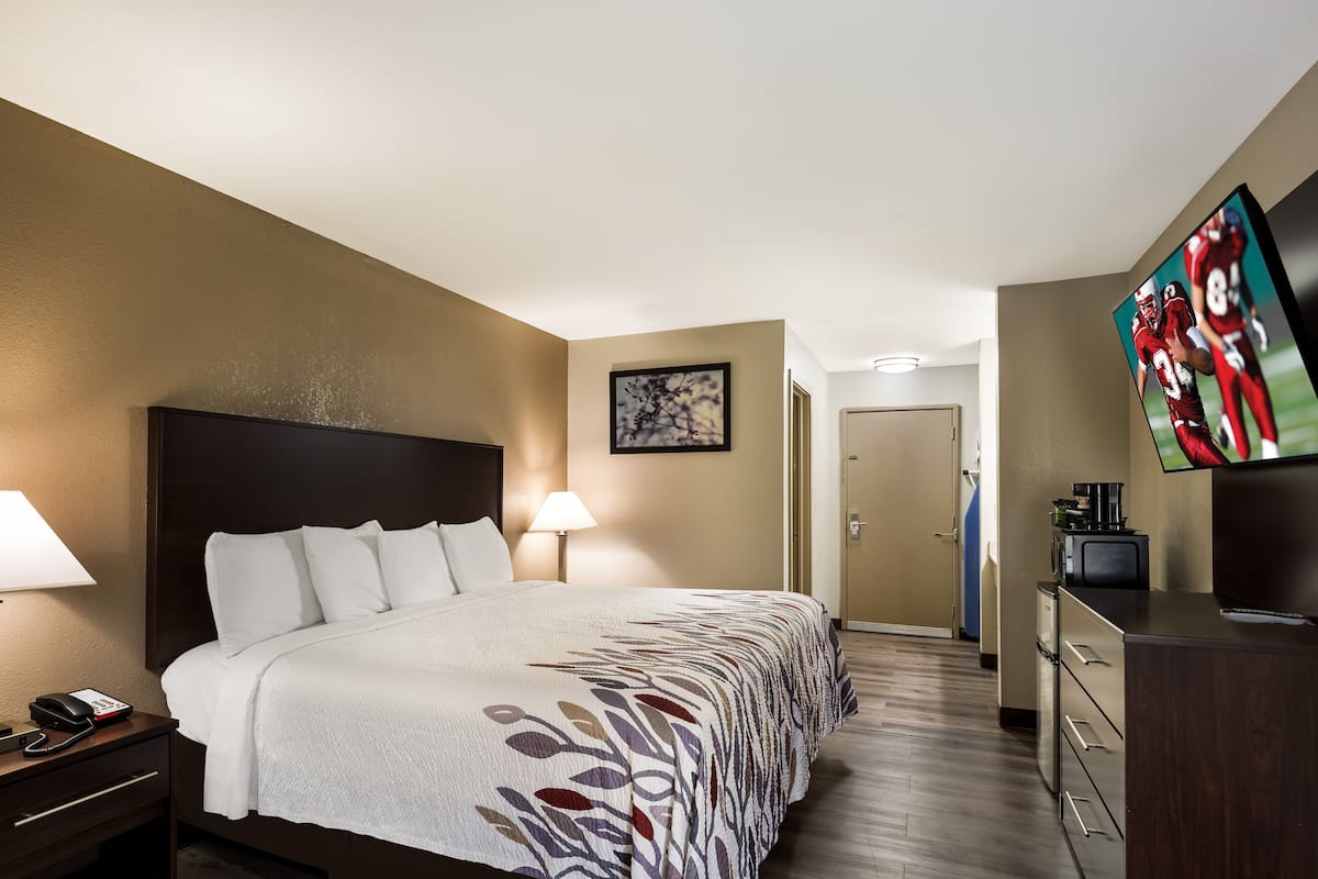 A hotel room with a large bed, bedside lamps, a flat-screen TV, a desk with a coffee maker, and a framed picture on the wall.