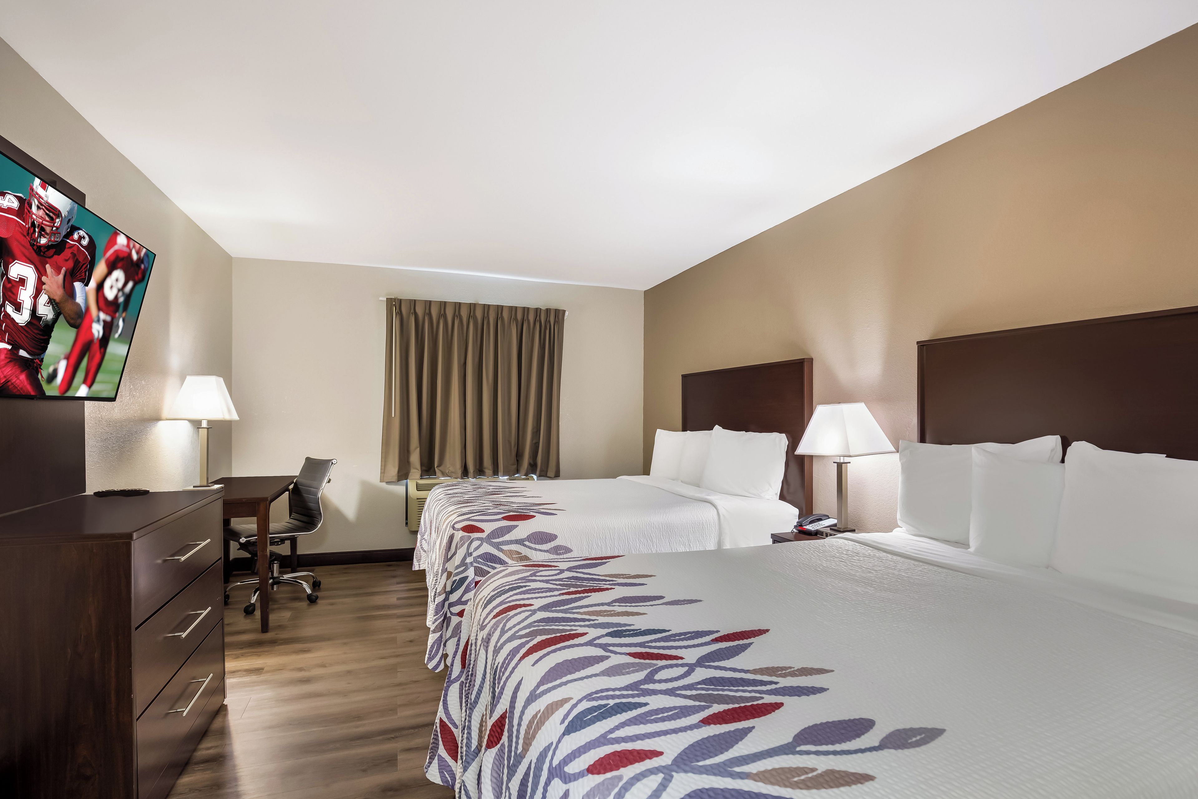 A hotel room with a bed, desk, chair, and a television on the wall.
