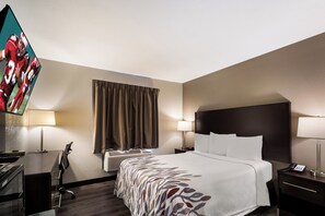 Een hotelkamer met een bed, nachtlampjes, een bureau met een computer, een televisie en een raam met gordijnen.