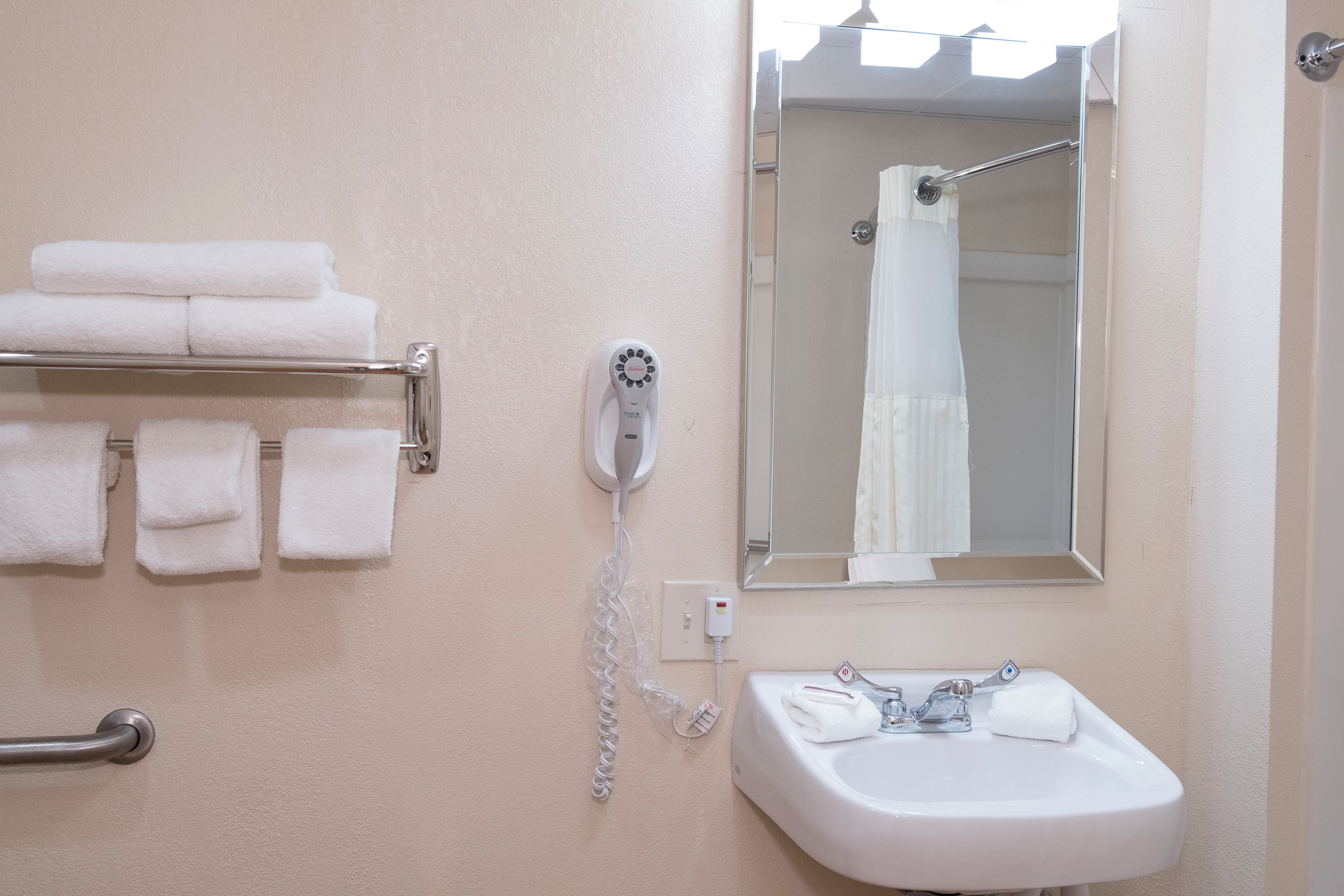 A bathroom with a sink, a mirror, a towel rack with folded towels, and a shower with a curtain.
