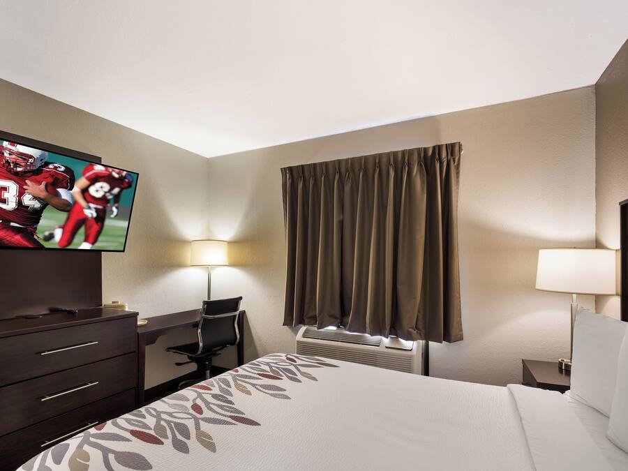 A hotel room with a bed, a desk, a television, a lamp, and a window with curtains.