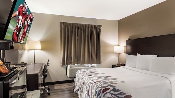 A hotel room with a bed, two bedside lamps, a television, a desk with a lamp, a chair, and a window with curtains.