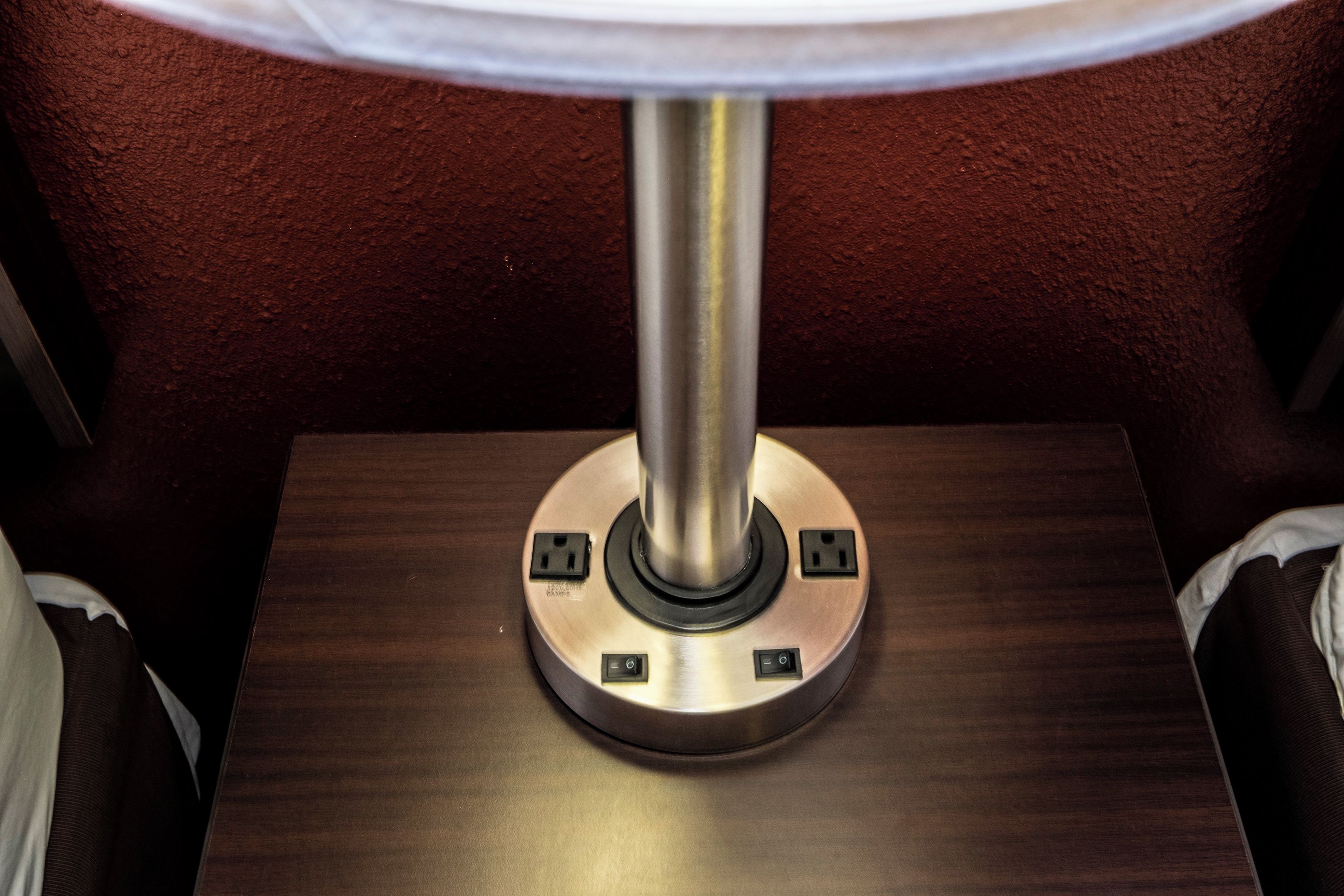 A table lamp with a metallic base and two electrical outlets on a wooden surface.