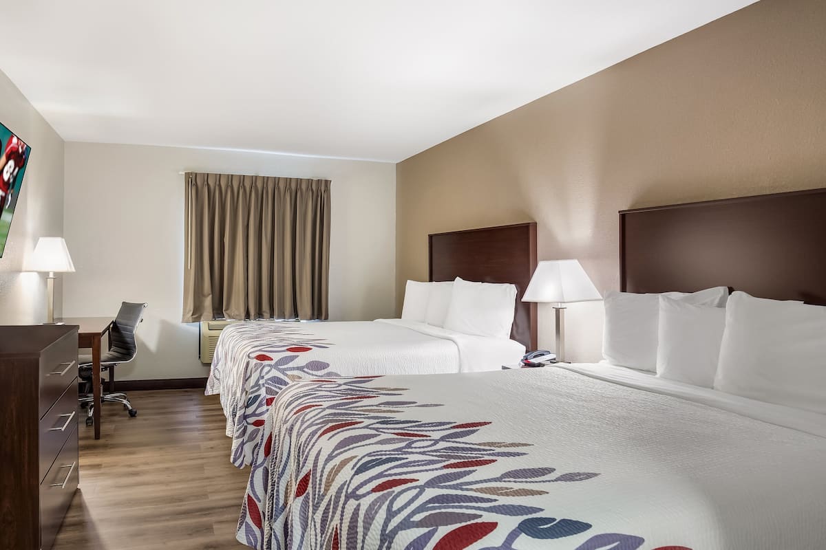 A hotel room with a bed, bedside lamps, a desk with a chair, and a TV on the wall.