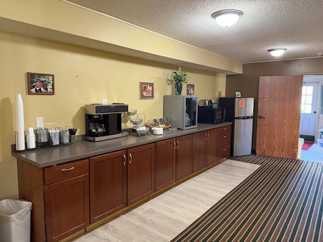 A kitchen with a coffee machine, microwave, refrigerator, and a striped rug.