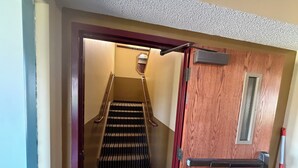 A wooden door with a metal handle and a window, leading to a carpeted staircase with a handrail.