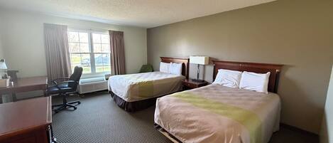 A hotel room with two beds, a desk, a chair, and a window with curtains.