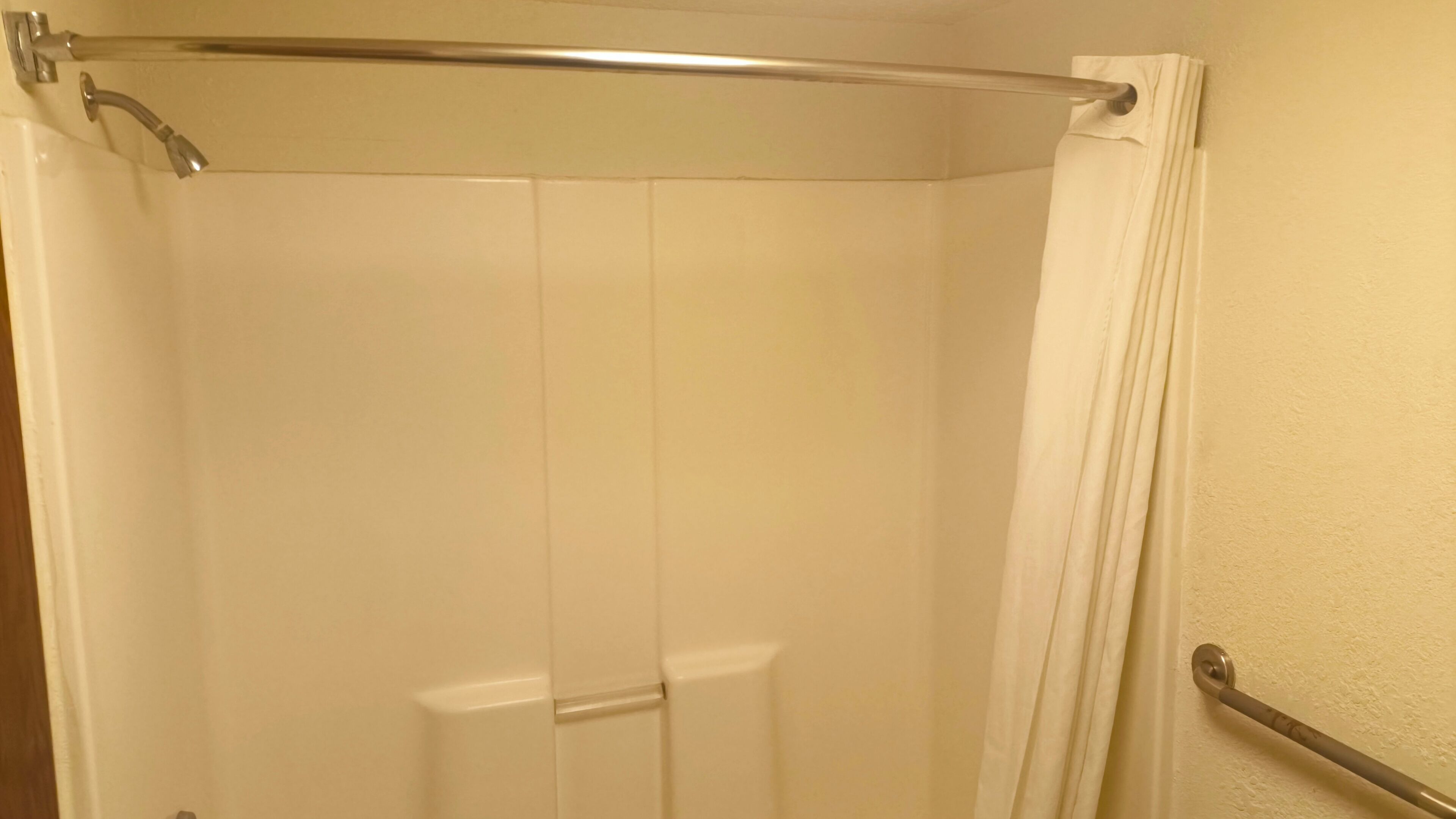 A shower enclosure with a glass door, a metal grab bar, and a white curtain.