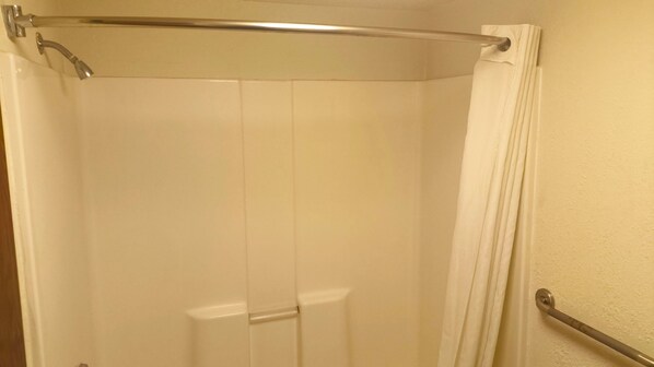A shower enclosure with a glass door, a metal grab bar, and a white curtain.