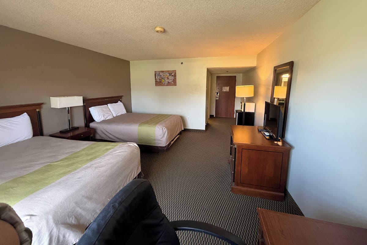 A hotel room with two beds, a desk, a chair, a TV, and a mirror.